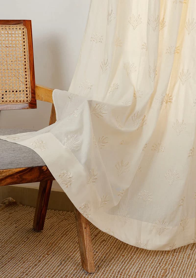 Ivory cotton curtain with delicate tonal floral embroidery draped over a cane chair