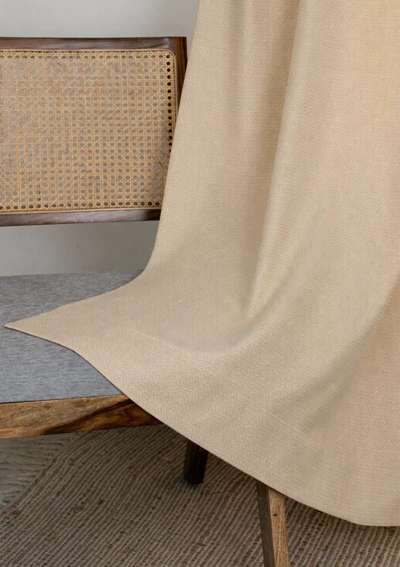 Vanilla-beige textured cotton curtain draped over a cane chair